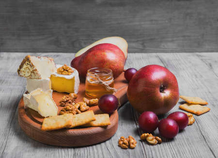 Fruit pear whole, grapes, pear cut in half, cheese, camembert cheese, goat cheese, honey, walnuts on a light white wooden backgroundの写真素材