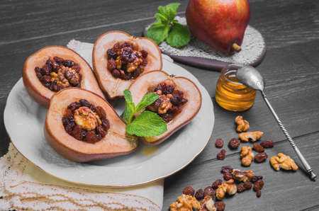 Sweet Baked pear halves with stuffing, ingredients for baked raisins, walnuts, honey, mint leaves, fresh pear, silver teaspoon, dark black wood background, white porcelain plate, ceramic board, lace doilyの写真素材
