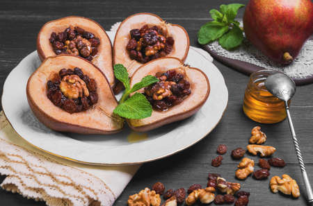 Sweet Baked pear halves with stuffing, ingredients for baked raisins, walnuts, honey, mint leaves, fresh pear, silver teaspoon, dark black wood background, white porcelain plate, ceramic board, lace doilyの写真素材
