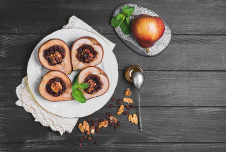 Sweet Baked pear halves with stuffing, ingredients for baked raisins, walnuts, honey, mint leaves, fresh pear, silver teaspoon, dark black wood background, white porcelain plate, ceramic board, lace doily, top viewの写真素材