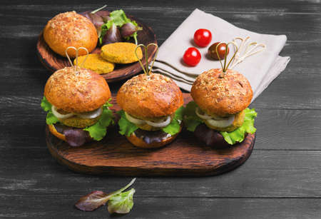 Vegan burgers with vegetables, onion, vegetable cutlets, lettuce, sauce, ingredients for cooking vegan burgers cherry tomatoes, lettuce, rolls, skewers on a wooden surface of a dark black backgroundの写真素材