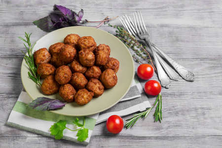 Small meat balls on a green plate, fresh herbs thyme, coriander, basil, rosemary, cherry tomatoes, napkin, silver fork on a light white wooden background in rustic styleの写真素材