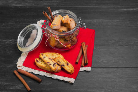 Italian biscotti cookies in a glass jar, cinnamon sticks, cookies biscotti scattered on a red lacy...