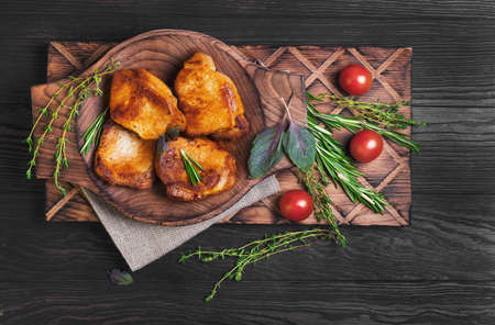 Meat fried pork steak baked, fresh green basil spices, thyme, rosemary, cherry tomatoes, burlap, brown dark wooden background in rustic style, top viewの写真素材