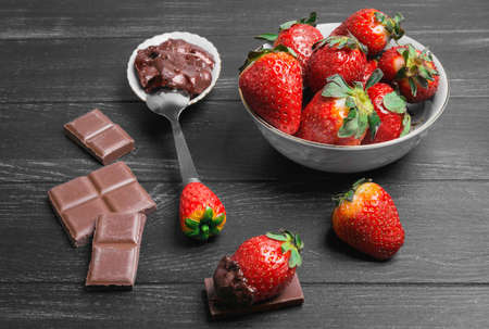 strawberries in white plate, milk chocolate bars, strawberries in chocolate spread on a black wooden background, top viewの写真素材