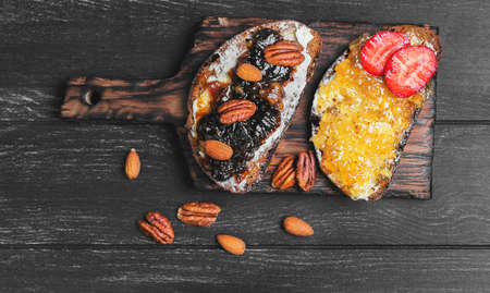 Sweet dessert sandwich crostini with lemon jam, sandwich with plums jam, nuts pecans, almonds, rye bread on a cutting board on a black wooden backgroundの写真素材