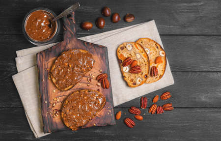 Sweet sandwiches with peanut butter, nuts almonds, pecans, chestnuts, served on the Board, on dark black surface wooden backgroundの写真素材