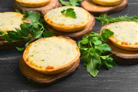 Little mini pizza tartlets with cheese and fresh herbs, lettuce, dill, parsley on a dark black background wooden surfaceの写真素材