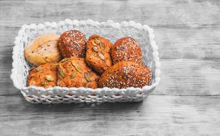 Three homemade rye buns with grit poppy, sesame and flax seeds, three rye buns with pumpkin seeds, homemade bun made with white flour in a white knitted basket on a light wooden background in the style of Shabby Chicの写真素材