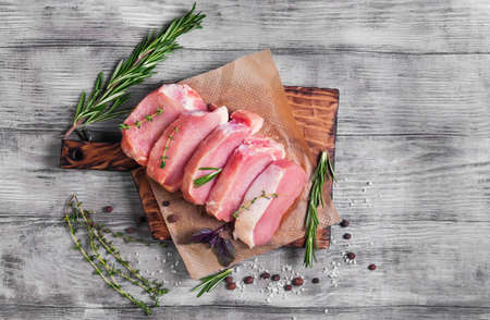 Pieces of raw pork steak with spices and herbs rosemary, thyme, basil, salt and pepper on a bright white wooden background in rustic style, top viewの写真素材