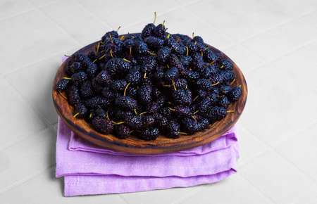 Fresh ripe mulberry berries in a black wooden plate on a white tableの写真素材