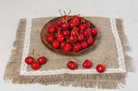 A wooden of rustic bowl full red berries cherries on lacy napkin of burlap on white table a few berries cherry nearの写真素材