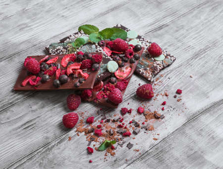 Tiles of a broken exquisite hand-made chocolate with red dried and fresh berries, chocolate with green Ingredients nuts, peel, mint, cocoa powderの写真素材