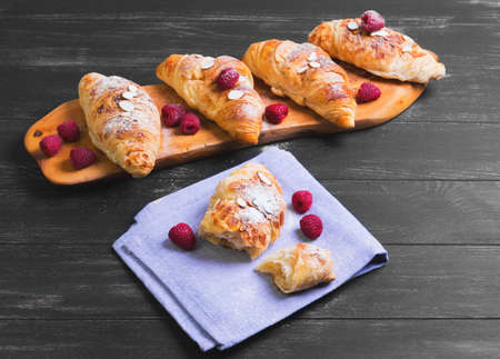 Break in half a croissant, four croissants on cutting board, raspberries berries, nuts, almonds, powdered sugar, napkin, black wooden backgroundの写真素材