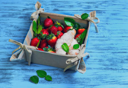 strawberries berries, baked two croissants with powdered sugar, lime leaves in a tissue box blue basket on worn wooden background surfaceの写真素材
