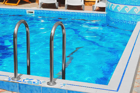Outdoor blue pool of water lined with decorative tiles, handrails metal, mosaic tile pattern, white...