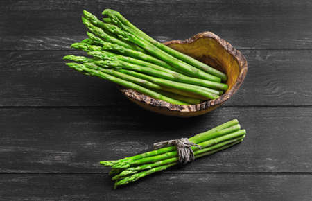 Asparagus green on dark black background wooden surface, asparagus beam tied with rope and twine in wooden bowl especially for asparagus, handmade from olive woodの写真素材