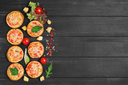 Small pizza with mozzarella cheese, sausage, ham, parsley, lettuce, cherry tomatoes on dark black wooden background, empty form, place for text, recipeの写真素材