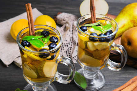 Two pears cocktails in glasses, ingredients for cocktails and fresh whole fruit pears, lemons, blueberries, mint leaves, cinnamon sticks, burlap cloth, wooden board on dark backgroundの写真素材
