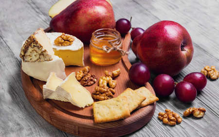 Fruit pear whole, grapes, pear cut in half, cheese. Camembert cheese, goat cheese, honey, walnuts on light white wooden backgroundの写真素材