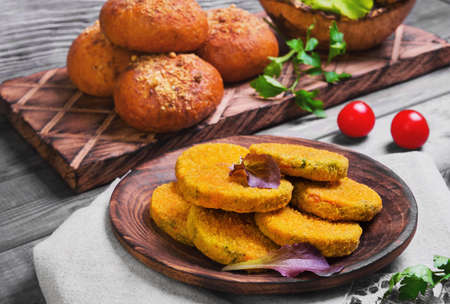 Vegetarian food vegetable cutlets for burgers, parsley, cherry tomatoes, lettuce, bread buns for burgers, wooden dish, gray background in rustic styleの写真素材