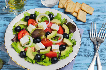 Vegetarian meal salad of avocado, olives, onions, cherry tomatoes, feta cheese, lettuce, avocado oil, salt, bread, crackers on napkin blue wooden backgroundの写真素材
