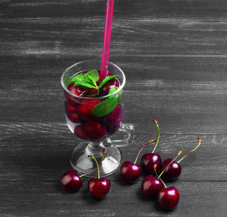 Cocktail with fresh sweet cherries, black cherry berries, mint and straw on dark wooden background in rustic styleの写真素材