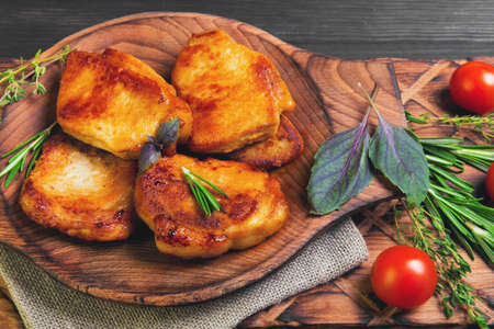 Meat fried pork steak baked, fresh green basil spices, thyme, rosemary, cherry tomatoes, burlap, brown dark wooden background in rustic styleの写真素材