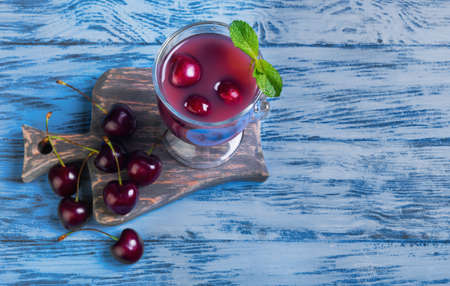 Summer fruit cocktail with fresh sweet cherries, black cherry berries, mint, glass, board on blue wooden background in rustic style, top viewの写真素材