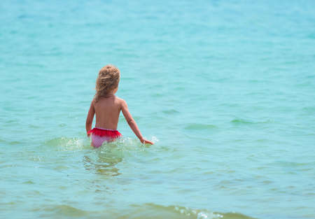 A little girl walks into the sea in swimming shortsの写真素材