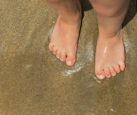 Standing feets foot little child baby on wet sea sand goldenの写真素材
