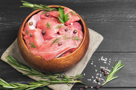 Slices of pork stew in wooden bowl on sacking with spices and herbs on black wooden backgroundの写真素材