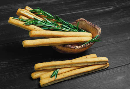 Crispy bread sticks with thyme and rosemary in a wooden bowl, bread sticks on black wooden table, black backgroundの写真素材
