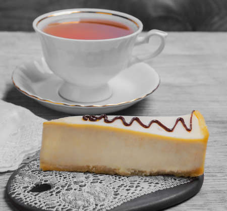 Cake Cheesecake classic New York, decorated with chocolate, white cup of black tea cloth on light wooden background surfaceの写真素材