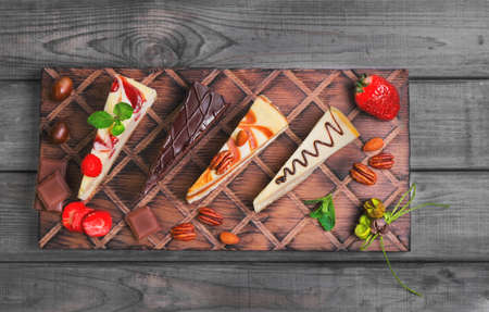 Assorted cakes cheesecake strawberry, caramel, chocolate, caramel, cut into pieces on wooden board,...