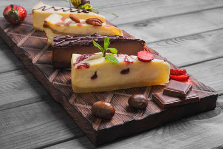 Assorted cakes cheesecake strawberry, caramel, chocolate, caramel, cut into pieces on wooden board, fresh berries strawberry, nuts chestnuts, almonds, pecans, leaves mint, gray wooden backgroundの写真素材