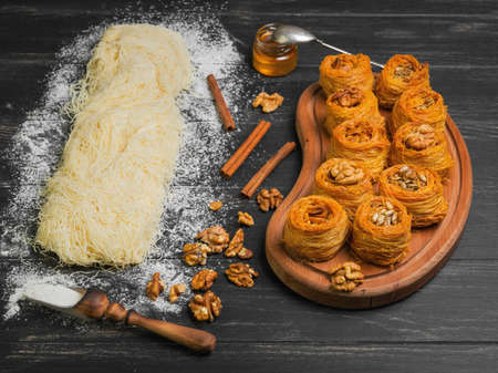 Cooking sweets turkish traditional ramadan pastry dessert kunafa kadaif, baklava , ingredients dough, nuts, walnuts, peanuts, sunflower seeds, honey, cinnamon, dark black wood backgroundの写真素材