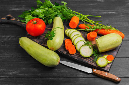 Vegetables ingredients for vegetable dishes. Vegetables marrows white squashes, carrots, parsley, lettuce, dill, tomato. Marrows white squashes, carrots whole and cut into pieces. The dark black wood background.の写真素材