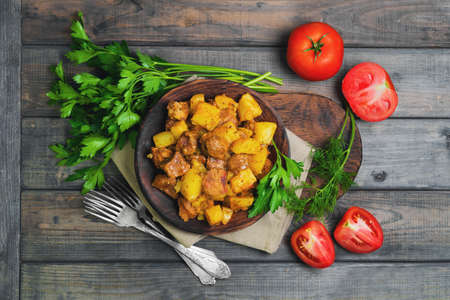 Stewed potatoes with meat Goulash , additional ingredients for stewed with potatoes tomatoes, dill, parsley, gray wooden background, top viewの写真素材