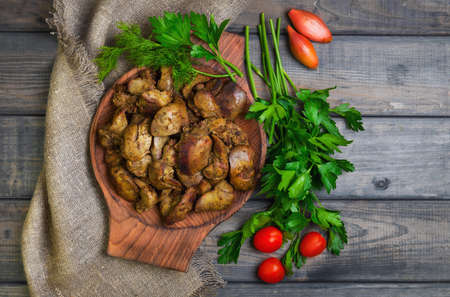 Stewed chicken liver, additional ingredients for chicken liver parsley, dill, cherry tomatoes, shallot, gray wooden background, rustic style, top viewの写真素材