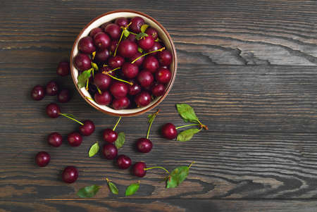 Red ripe cherries in bowl ceramic, red cherries on wooden table, green cherry leaves, brown wooden background, top viewの写真素材