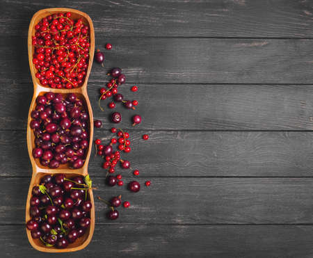 Garden fresh red berry fruit. Gooseberry, cherry, red currant. Red berries are scattered on dark wooden background black gooseberry, cherry, red currant. Top view.の写真素材