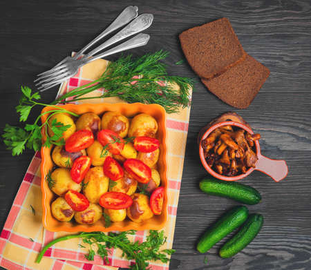 Autumn dinner Baked roasted young potatoes, tomatoes in ceramic form. Greens for baked roasted potatoes thyme, parsley, dill. Roasted with potatoes Chanterelle Mushrooms, dark wooden background. Top viewの写真素材