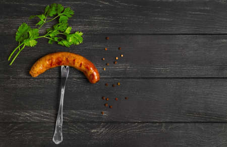 Meat Grilled homemade sausage on fork, spices for grilled sausage parsley, pepper peas, dark black wooden background. Empty place for text. Top view.の写真素材