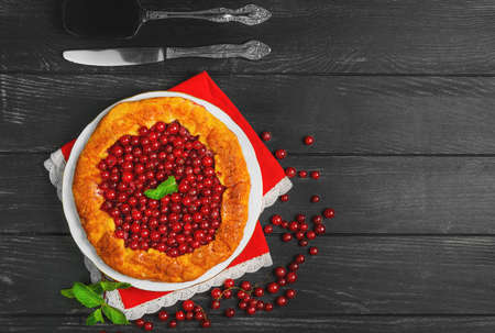 Open pies tart with berries red currant. Fresh red currant berries for Open pies tart, mint, red lace cloth. Dark black wooden background, top viewの写真素材