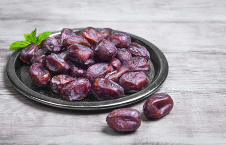 Side view of metal plate of Tunisian pitted dates, mint. Dried dates on wooden white table top backgroundの写真素材