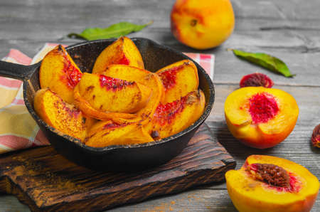 Baked peaches on a cast iron pan, leaf, cinnamon, spices for baked peaches. Fresh red fruit yellow peaches for baking, gray wooden background, board.の写真素材