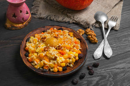 Pumpkin risotto with raisins. Rice porridge with sweet pumpkin, raisins, nuts, apricot. Fresh pumpkin for Halloween rice. Sacking, dark wood background.の写真素材