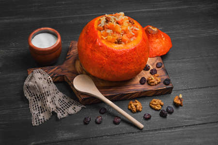 Pumpkin risotto with raisins. Rice porridge with sweet pumpkin, raisins, nuts. Baked pumpkin Halloween for rice. Sugar, dark wooden background.の写真素材