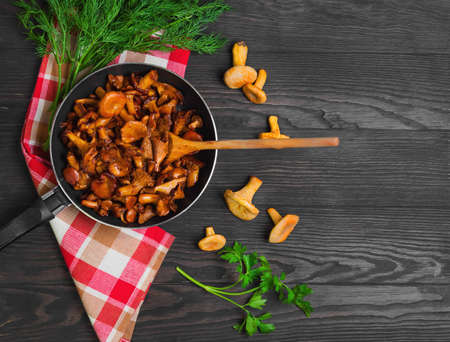 Chanterelle mushrooms fried in cast iron frying pan, herbs for roasted chanterelles parsley, dill, cloth. Raw chanterelles on a dark brown background of wooden table. Top view.の写真素材